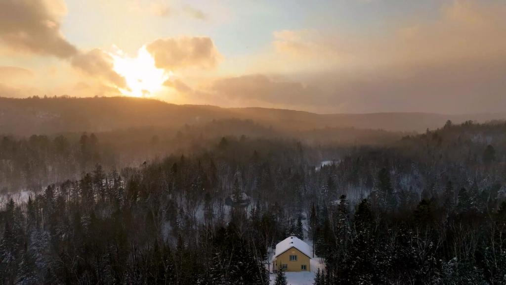 a house in the middle of a forest with the sunset at Chalet aux mille étoiles near Mt-Tremblant with Hot Tub in La Conception