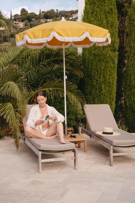 a woman sitting in a chair under an umbrella at Les Terrasses du Bailli in Rayol-Canadel-sur-Mer