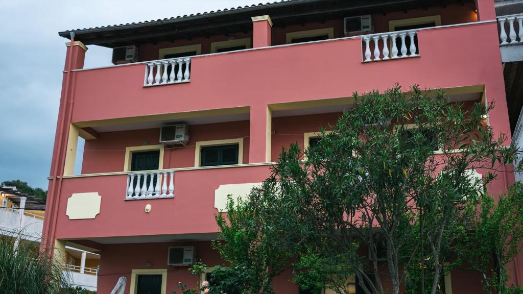 czerwony budynek z białym balkonem i drzewem w obiekcie Katerina Studios & Apartments w Sidari