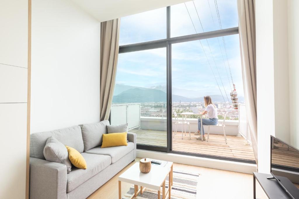 una mujer sentada en una silla en una sala de estar con una gran ventana en Les Appartements de Grenoble en Grenoble