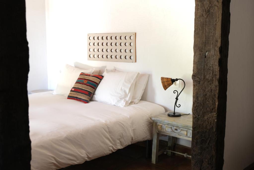 una cama con sábanas blancas y una lámpara sobre una mesa en The Wild Olive Andalucía Agave Guestroom en Casares