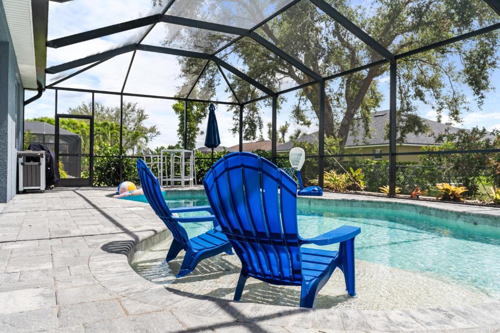 two blue chairs sitting next to a swimming pool at Beautiful Cape Coral Oasis! King Bed, BBQ, Heated Pool, PVT Yard & Much More! in Cape Coral