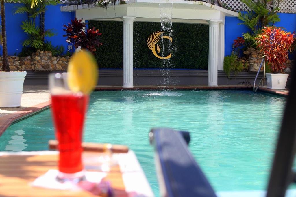 una bebida sentada en una mesa junto a una piscina en The Chancellor Hotel, en Puerto España