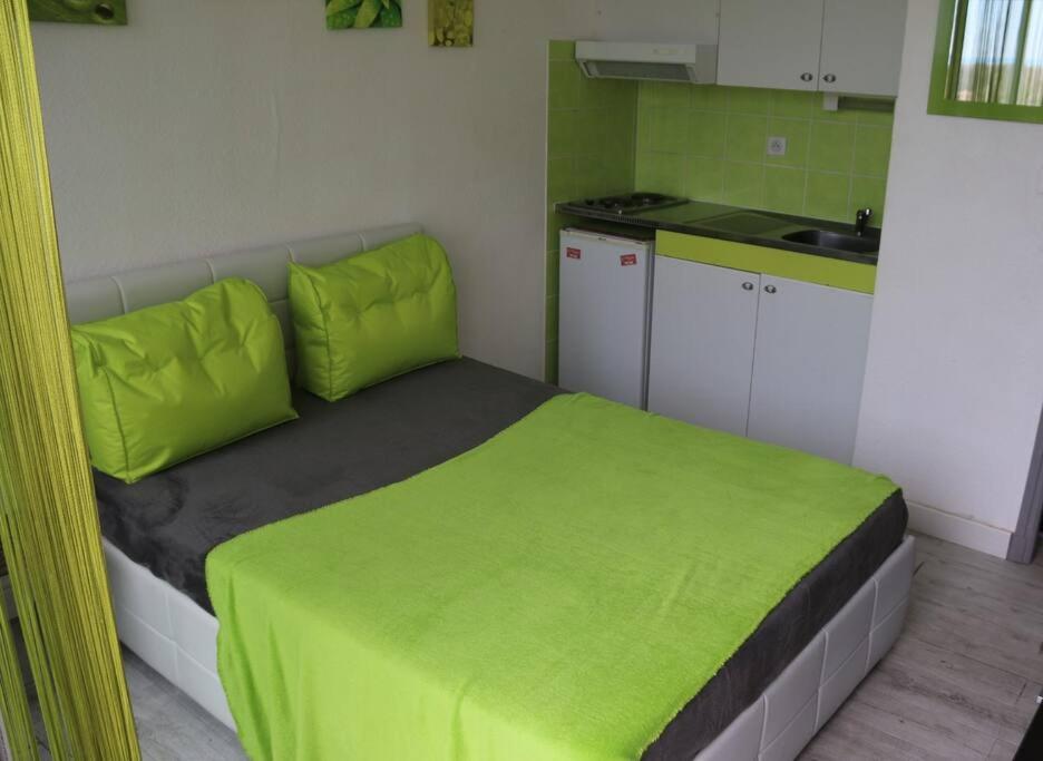 une petite chambre avec un lit avec des draps verts et une cuisine dans l'établissement Studio 23, Héliopolis L, village naturiste,, au Cap d'Agde