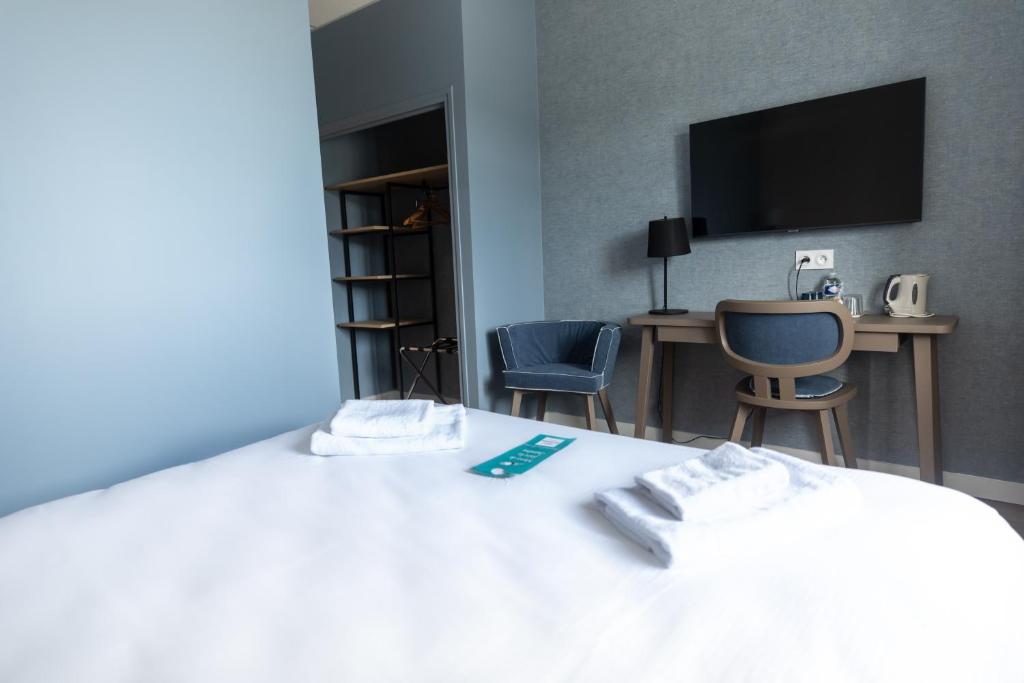 a bedroom with a bed with two chairs and a tv at Hôtel de la Baie in Crozon