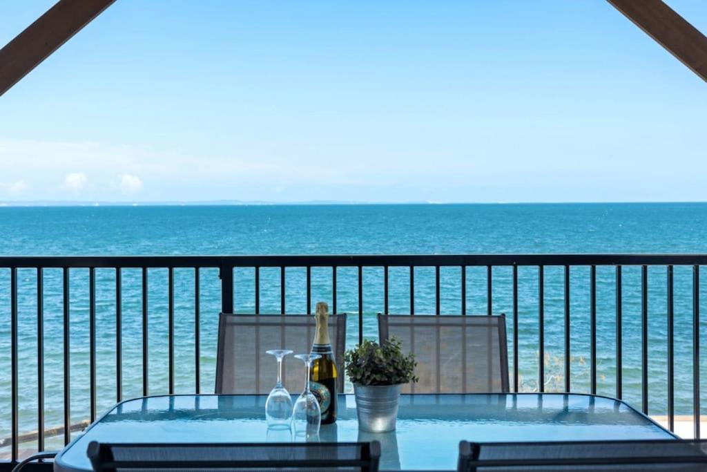 a table with a bottle of wine on a balcony with the ocean at Bay Vista Two Bedroom Waterfront Apartment in Redcliffe