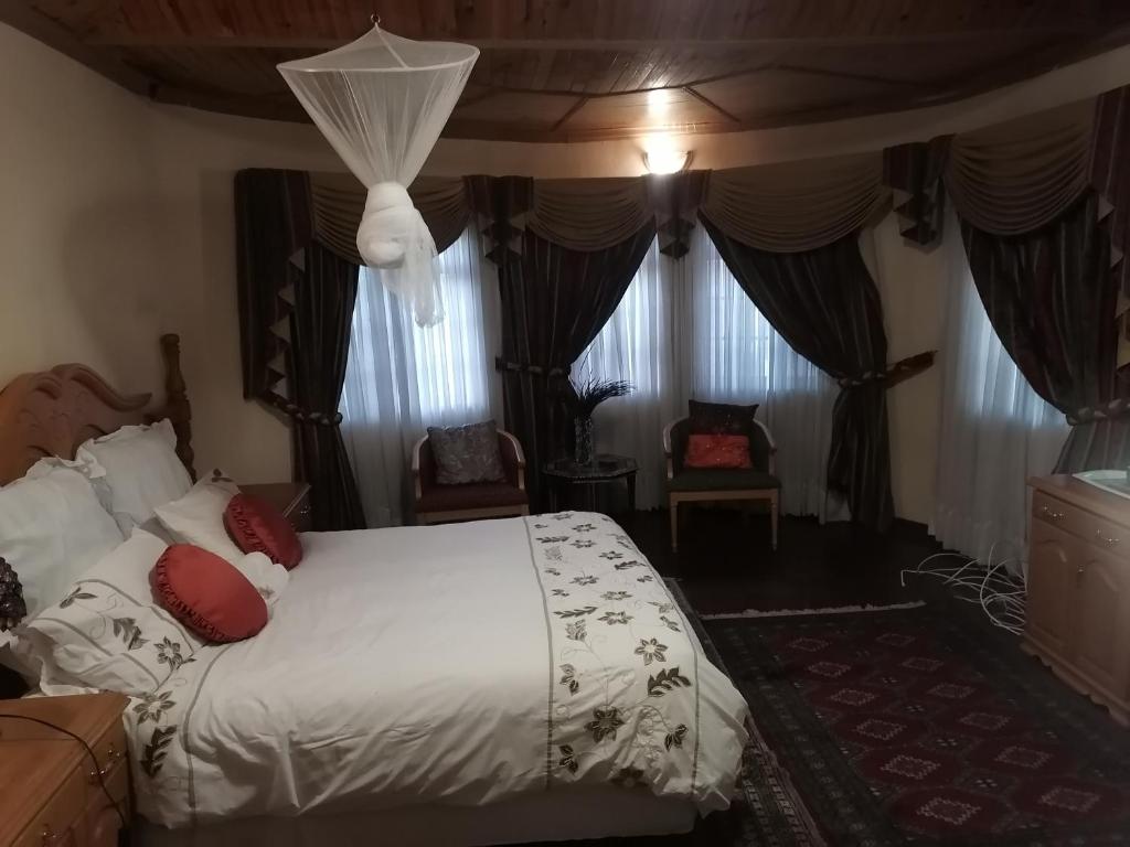 1 dormitorio con 1 cama con sábanas blancas y almohadas rojas en Tjibelu's Nest Guest Home en Lobatse