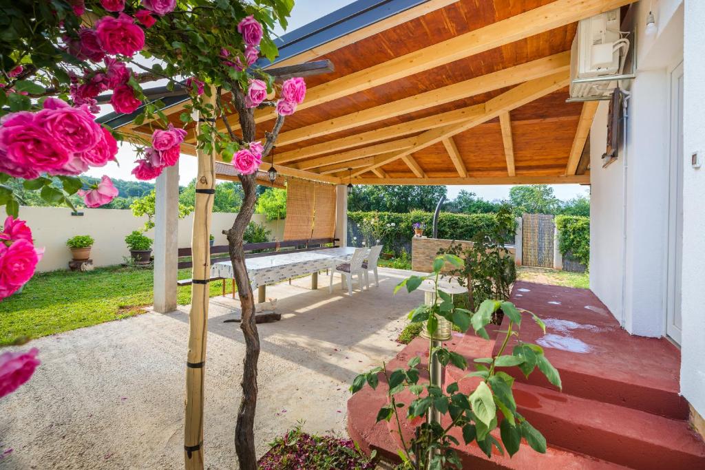 a wooden pergola with a bench and pink roses at Charming holiday house with beautiful garden and grill in Loborika