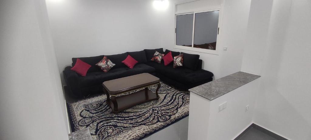 sala de estar con sofá negro y almohadas rojas en Logement familial 2, en Selouane
