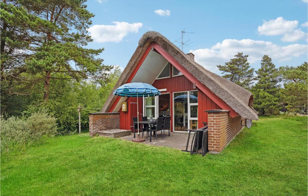 un cottage rosso con tetto di paglia, tavolo e ombrellone di Beautiful Home In Rm With 3 Bedrooms And Wifi a Rømø Kirkeby