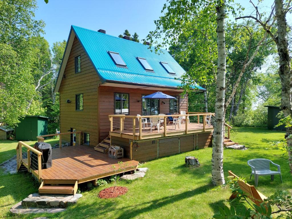 a house with a large deck and a blue roof at La Nef Bleu in Tadoussac