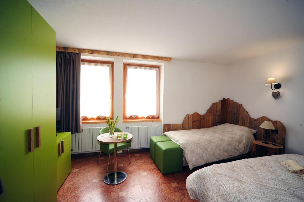 a bedroom with a bed and a table and two windows at Appartamenti e Camere Veronica in Cogolo