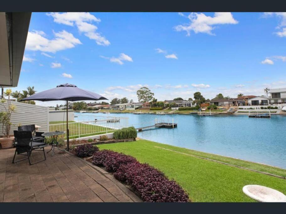a patio with a table and an umbrella next to a river at Waterfront Bliss in Port Macquarie