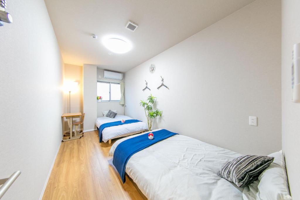 2 łóżka w pokoju z białymi ścianami i drewnianą podłogą w obiekcie GUEST House彩 w Osace