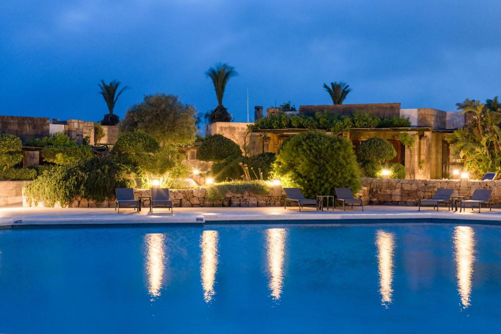 ein Pool mit Stühlen und ein Gebäude in der Nacht in der Unterkunft Hotel Ta' Cenc & Spa in Sannat