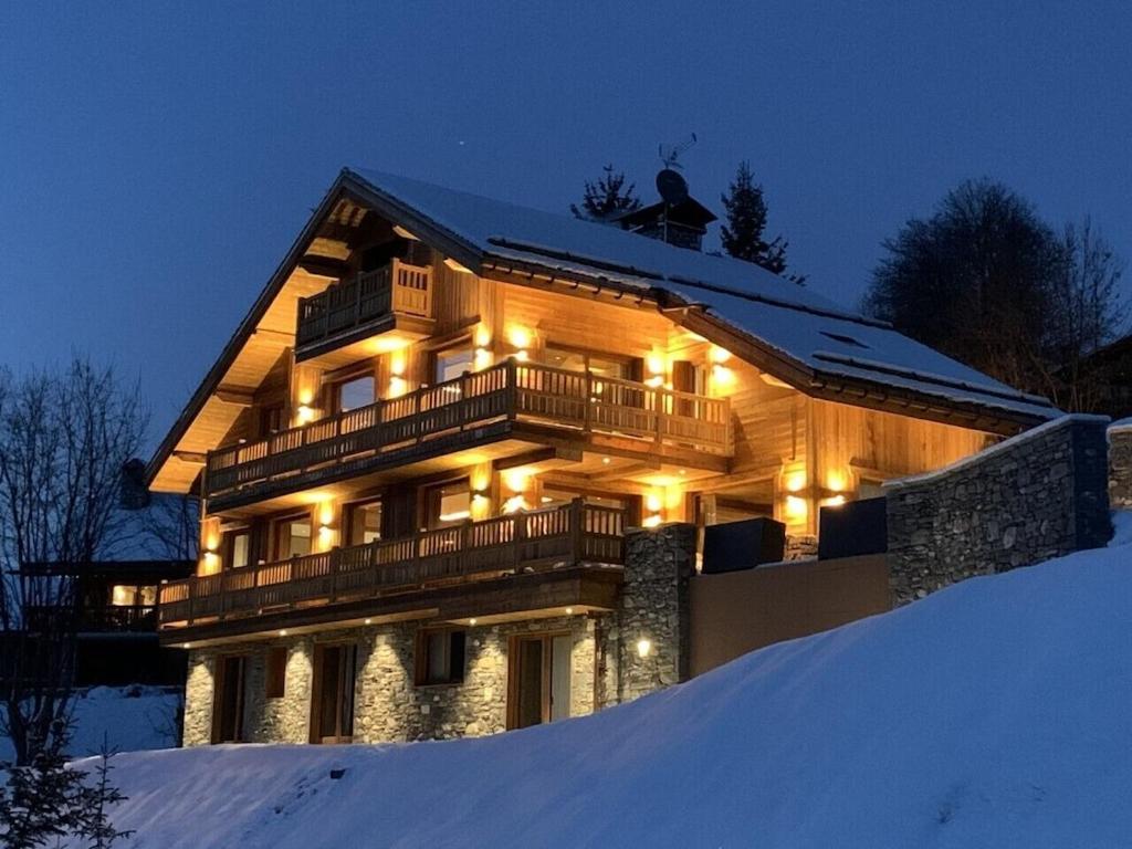 Une grande maison en bois avec des lumières dans la neige dans l'établissement Chalet Carriaz Meribel Village 14pers à 5min à pieds des pistes et commerces, à Les Allues
