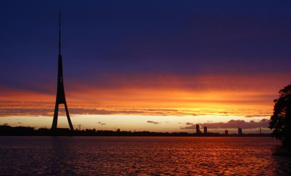 a sunset with a tower in the middle of the water at Krasta Home apartament Free Parking With CITY & RIVER VIEW in Rīga