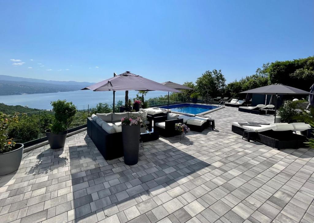 eine Terrasse mit Stühlen, einem Sonnenschirm und einem Pool in der Unterkunft Villa White Pearl Diamond Haus B, Opatija mit Meerblick & Pool in Opatija