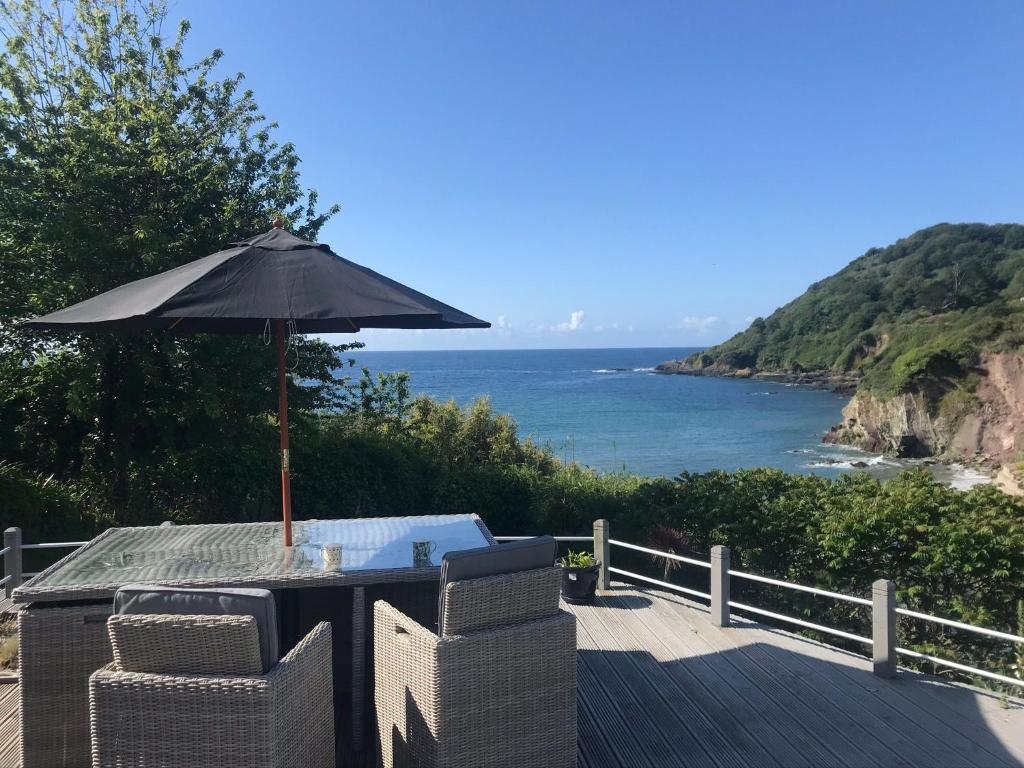 a table with an umbrella on a deck with the ocean at Beach Front House with Stunning Sea Views and Free Use of a Local Indoor Pool in Talland