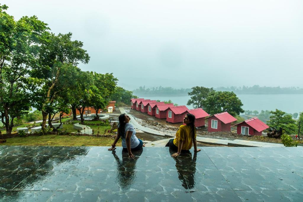 dos mujeres arrodilladas en el agua frente a las casas en The Hosteller Bhandardara en Bhandardara 
