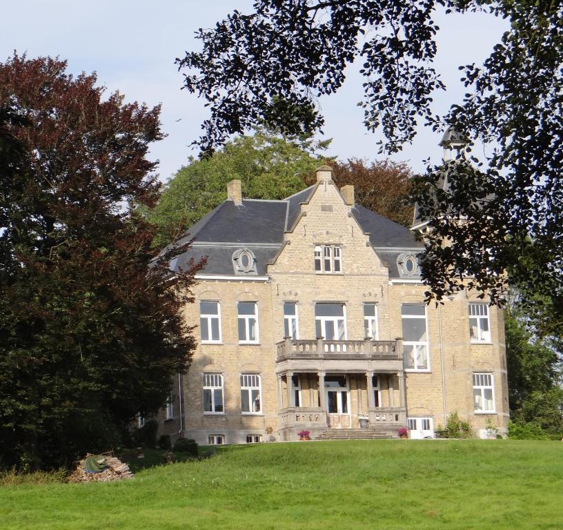 un grand bâtiment en briques sur une colline arborée dans l'établissement B&B Le Manoir de la Douve, à Heuvelland