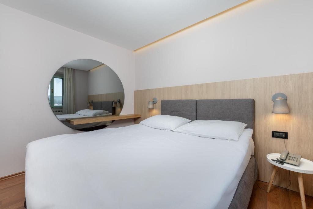 a bedroom with a large white bed and a mirror at Hotel Nostromo in Rabac