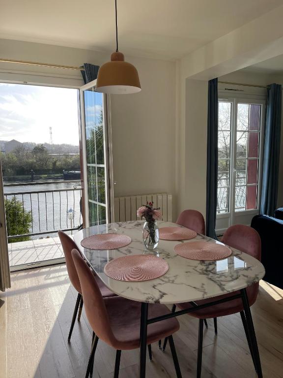 une salle à manger avec une table et des chaises et une fenêtre dans l'établissement Ambiance Seine, appartement surplombant la Seine -51 M2, Anémone-, à Thomery