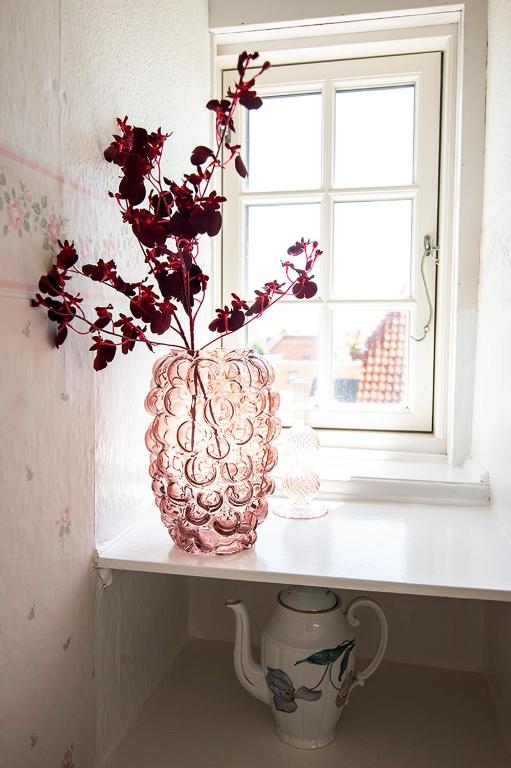 un vaso rosa seduto su uno scaffale vicino a una finestra di BO GODT I SKAGEN.DK a Skagen