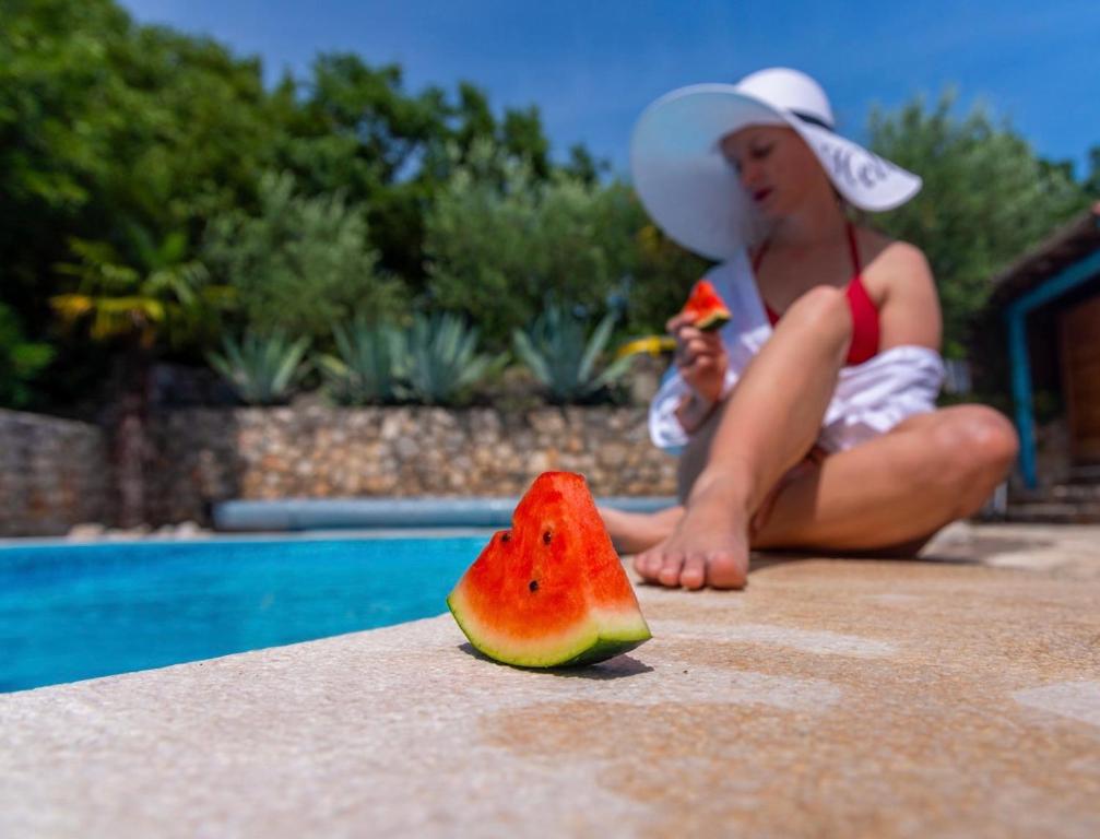 a woman sitting by a pool with a slice of watermelon at Apartments Villa Klaudia - Adults Only in Crikvenica
