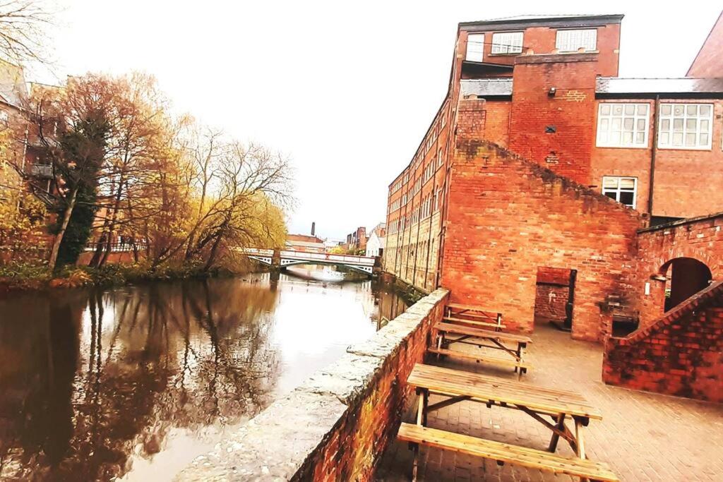 a river with two benches next to a brick building at Historic Kelham House with FREE on-site Parking in Sheffield