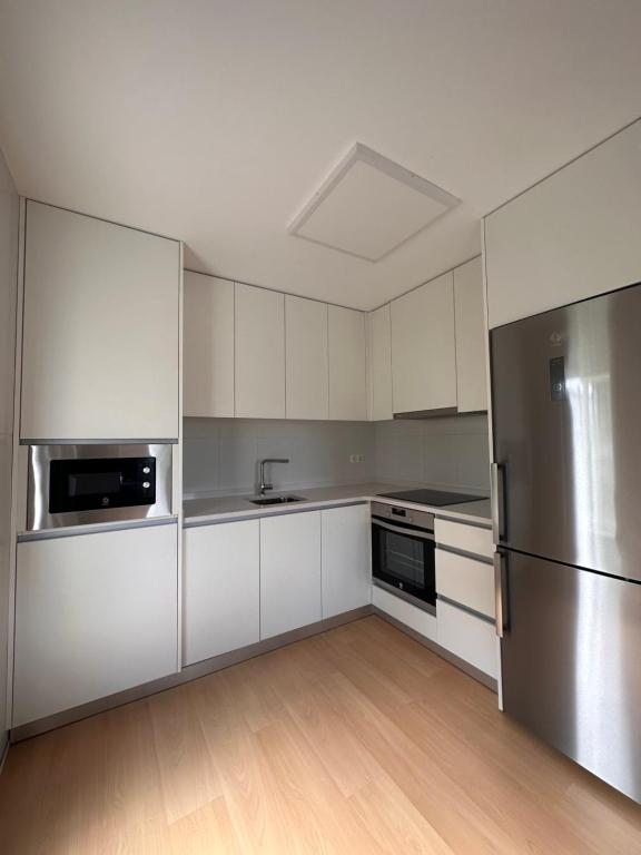 a kitchen with white cabinets and a stainless steel refrigerator at Aserradero - Bajo con terraza y piscina ! in San Martín de Arriba