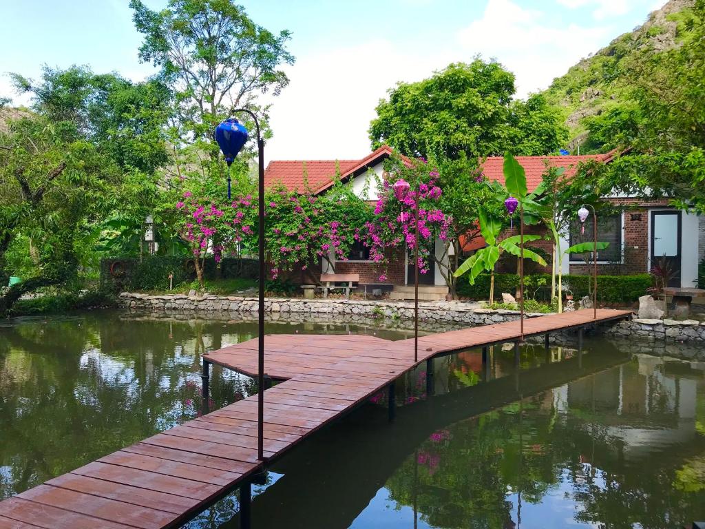 een houten brug over een rivier met roze bloemen bij Hang Mua Family Homestay in Ninh Binh