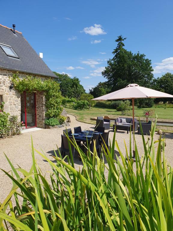 a patio with chairs and an umbrella and a building at Le Domaine de la petite chèvre in Ploumagoar