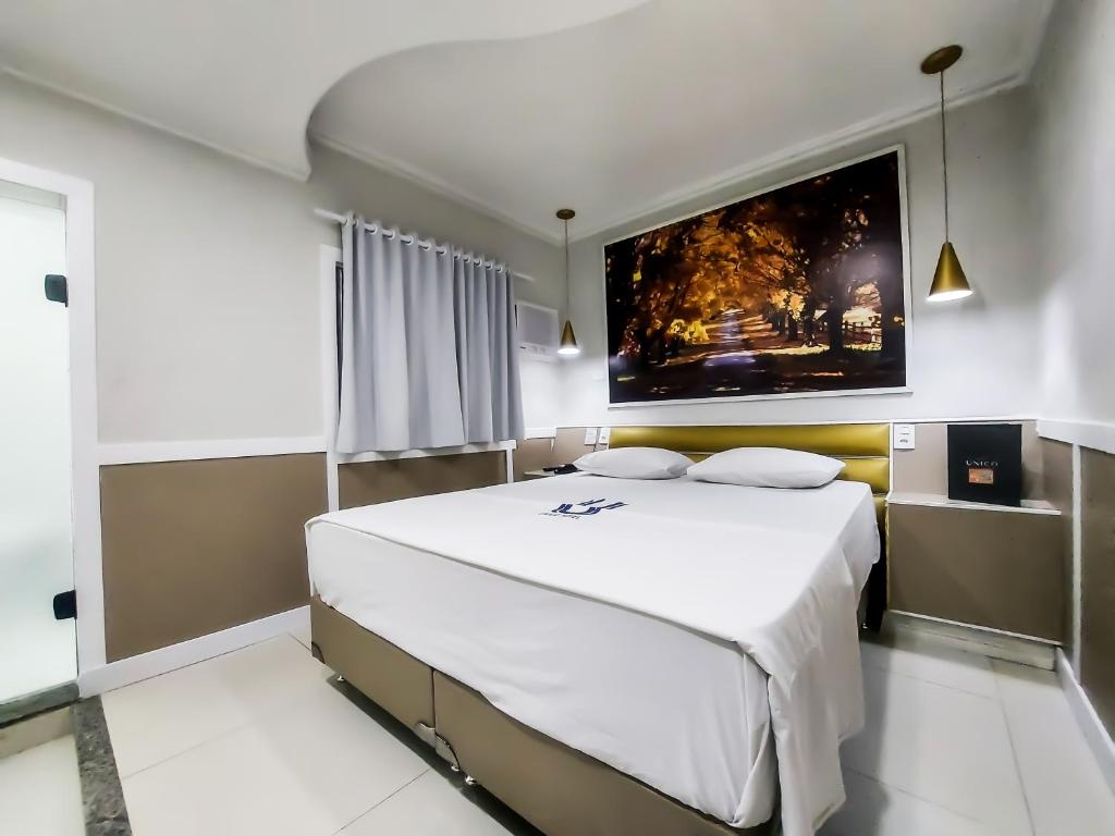 a bedroom with a large white bed with a painting on the wall at Calamares Hotel São Caetano in São Caetano do Sul
