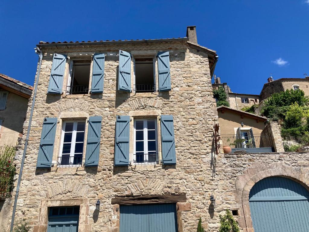un antiguo edificio de piedra con ventanas con persianas azules en le secret du chat, en Cordes-sur-Ciel