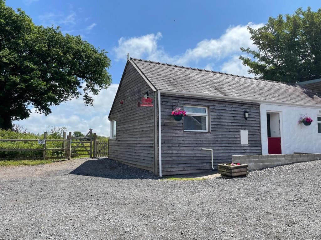 Un pequeño edificio con una puerta roja en un lote de grava. en Dairy Cottage, en Whitland