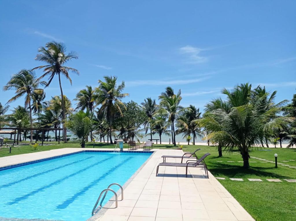 a swimming pool with palm trees and the ocean at Bangalô 7b Praia de Guaratiba in Prado