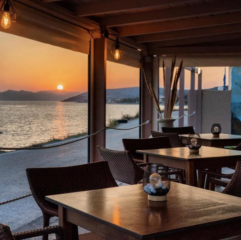 Sunset Sea View في Elíka: مطعم به طاولات وكراسي مع غروب الشمس في الخلفية