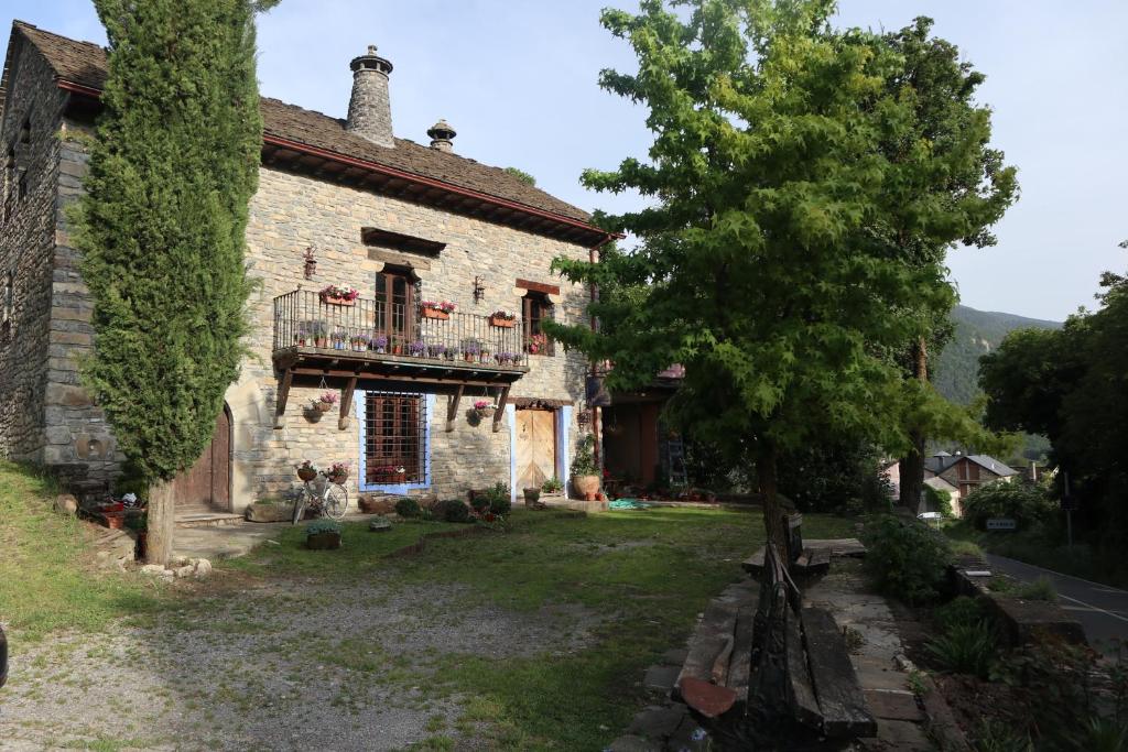 uma antiga casa de pedra com uma varanda e uma árvore em Casa María Berna em Sarvisé