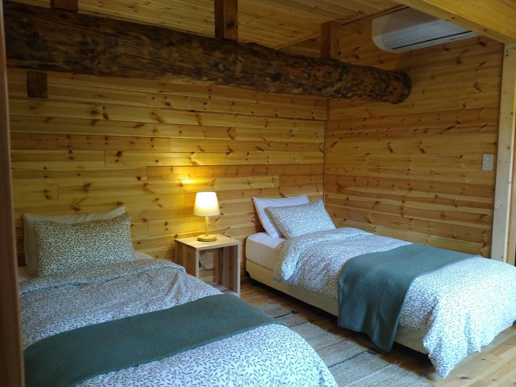 two beds in a room with wooden walls at Robin's Lodge in Iiyama