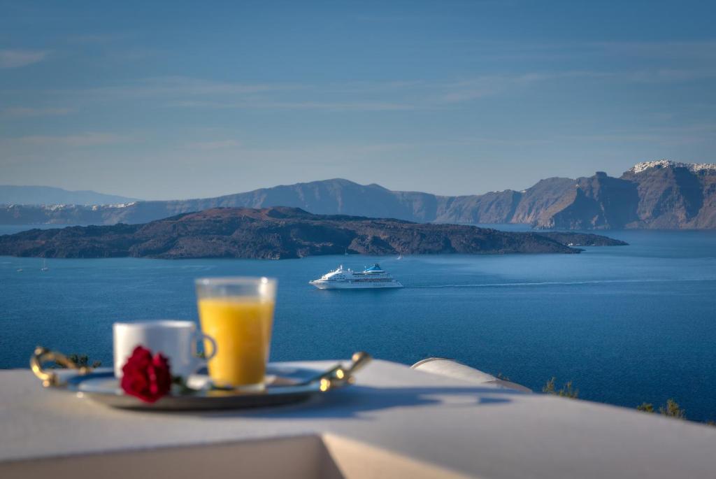 a glass of orange juice on a table with a boat in the water at William's Houses in Akrotiri