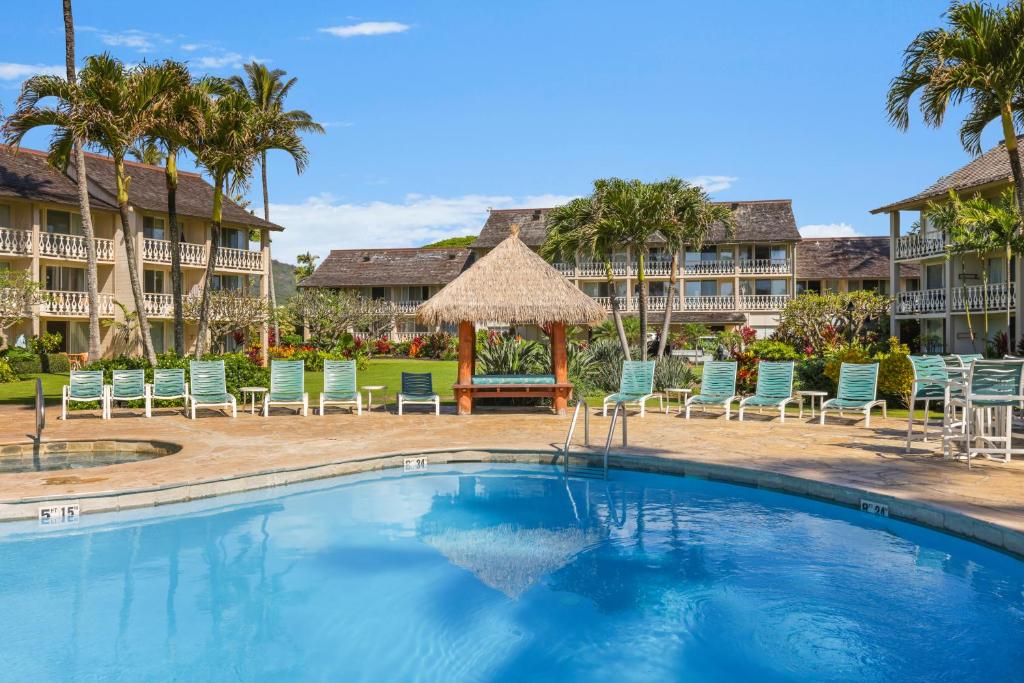 a swimming pool at a resort with chairs and an umbrella at Aston Islander On The Beach in Kapaa