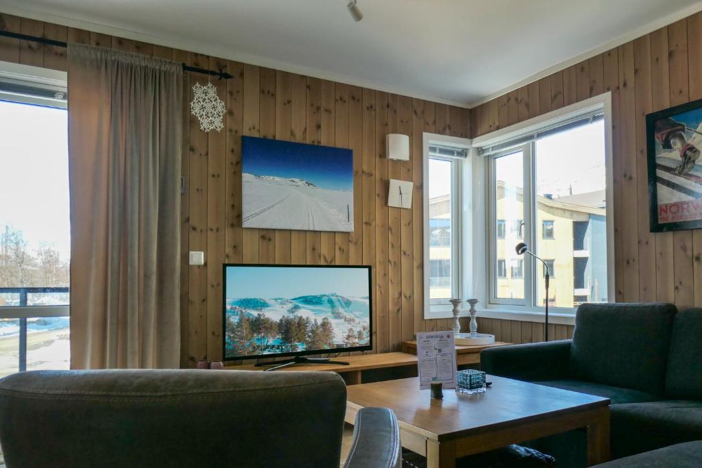 uma sala de estar com uma televisão, um sofá e uma mesa em Slåttastølen leiligheter - by Geilolia em Geilo