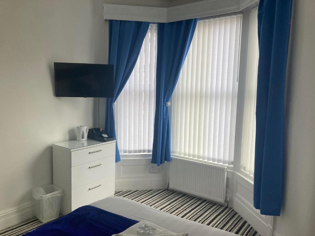 a bedroom with blue curtains and a bed and a dresser at The New Astoria Hotel in Blackpool