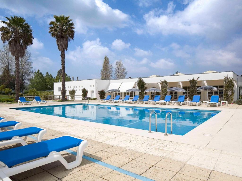 uma grande piscina com cadeiras azuis e palmeiras em Novotel Setubal em Setúbal
