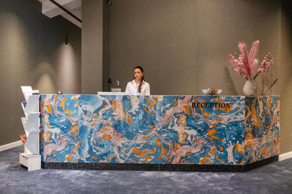 a woman standing behind a large painting of mermaids at Nam Hotel in Prizren