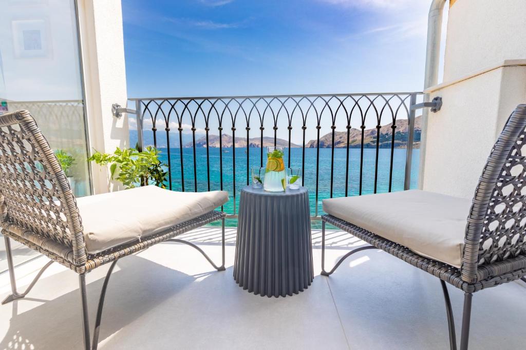 two chairs and a table on a balcony with a view of the water at Seafront Baska Apartment in Baška