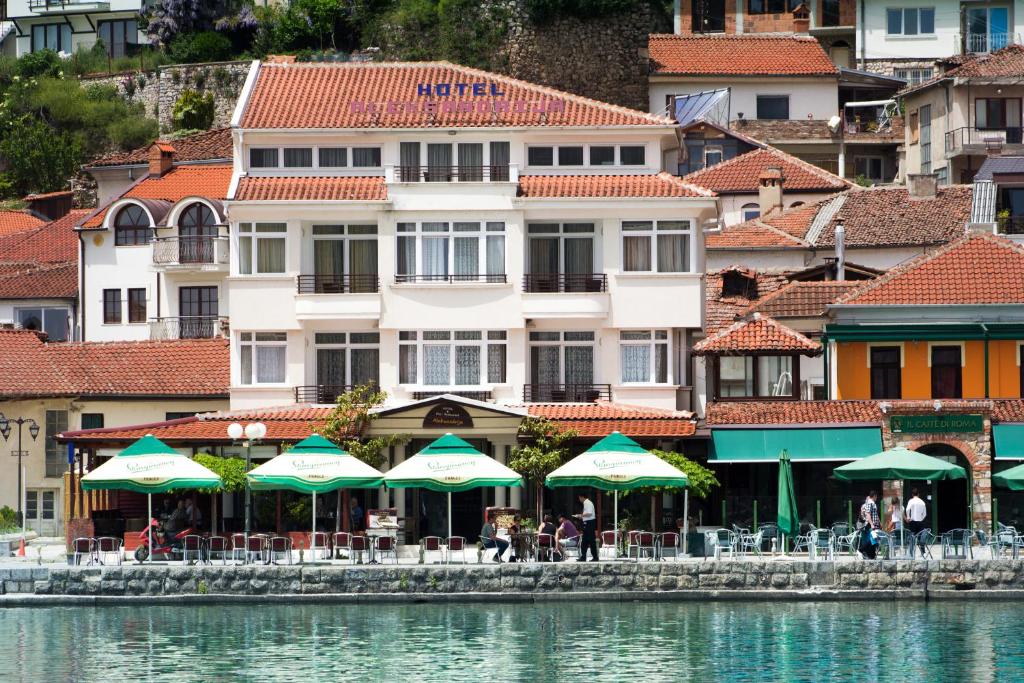 a building with tables and umbrellas next to the water at Hotel Aleksandrija in Ohrid
