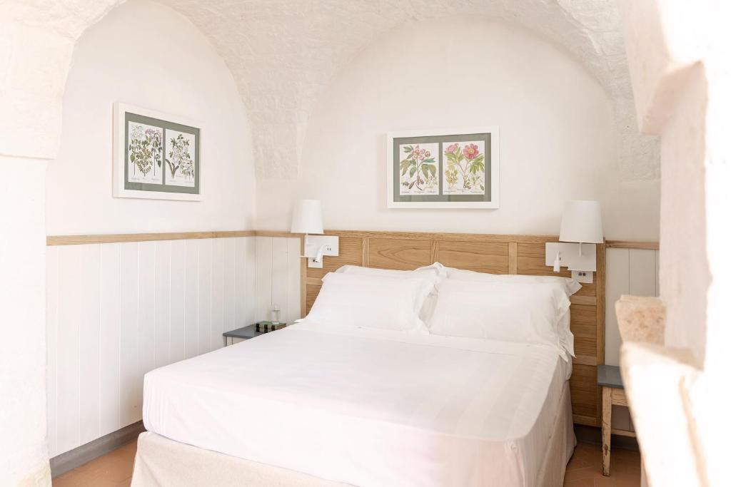 a white bed in a room with two pictures on the wall at Masseria Auraterrae in Polignano a Mare