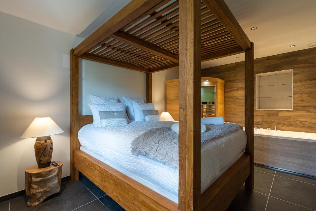 a bedroom with a wooden canopy bed with blue pillows at Géraniums Et Neige Fraîche, Maison d'Hôtes avec Suites Haut de Gamme, Balnéo massante et Sauna privés in Métabief